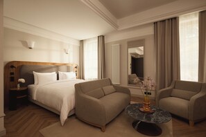 Habitació d'hotel amb llit, dos seients, taula rodona petita, mirall i radiador.