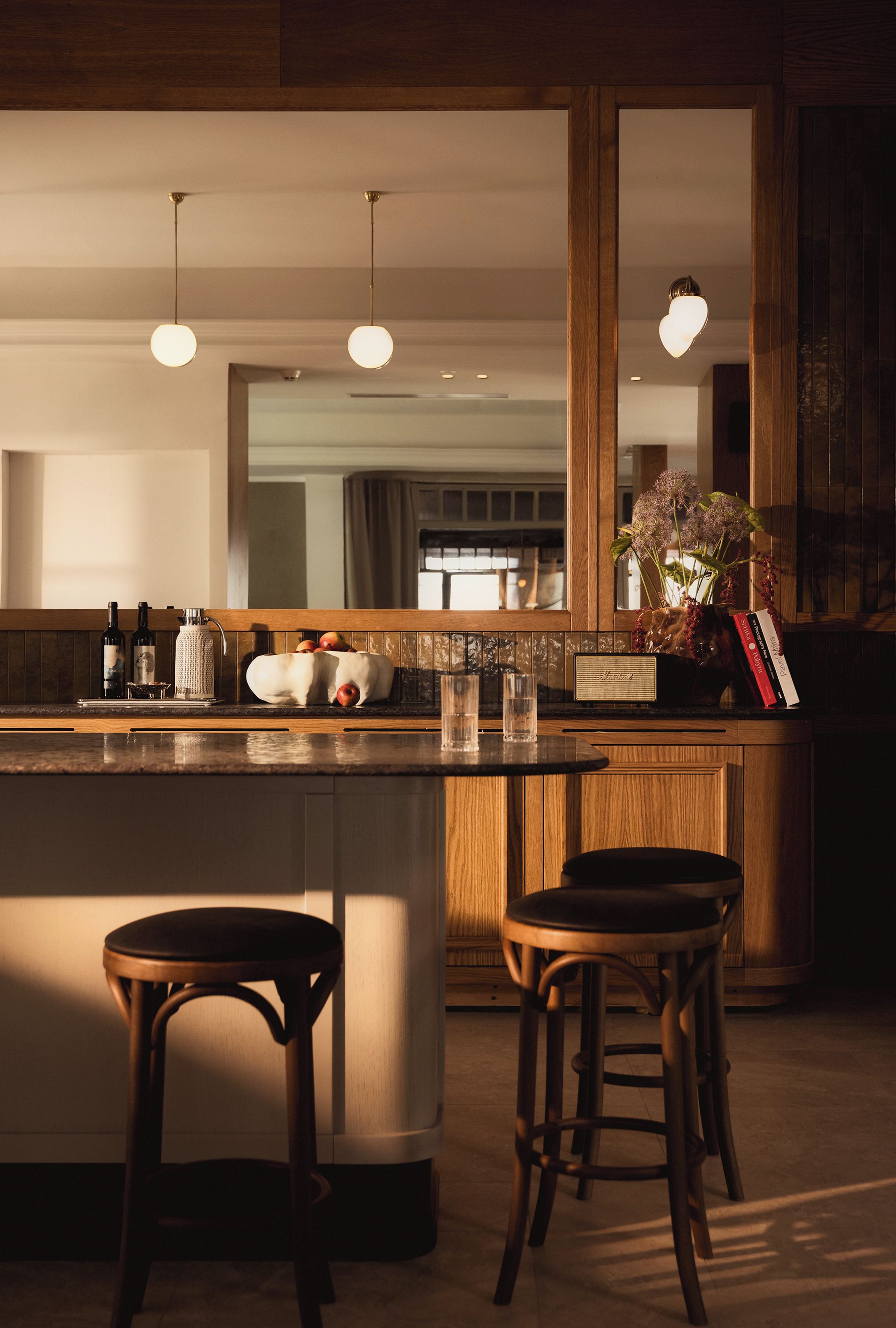 Una cocina moderna con una isla central, taburetes de bar, iluminación colgante y un espejo grande sobre la isla.