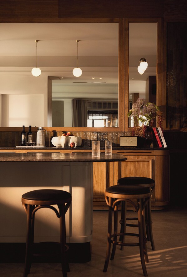 A modern kitchen with a central island, bar stools, pendant lighting, and a large mirror above the island.