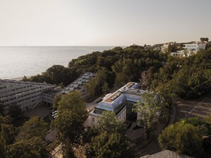 A coastal building complex with multiple structures, including a large building with a flat roof and smaller buildings with sloped roofs.