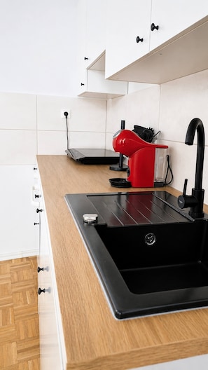 A modern kitchen with a black sink, wooden countertop, white cabinets, and a red kettle. - Spacious 125m² Apartment in Gera City Center for 8 Guests (Gera)
