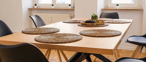 A dining area with a wooden table, black chairs, woven placemats, and a potted plant.