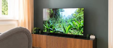Una sala de estar moderna con un televisor de pantalla plana montado en un mueble de madera, un sillón gris y una cabeza de ciervo decorativa en la pared.