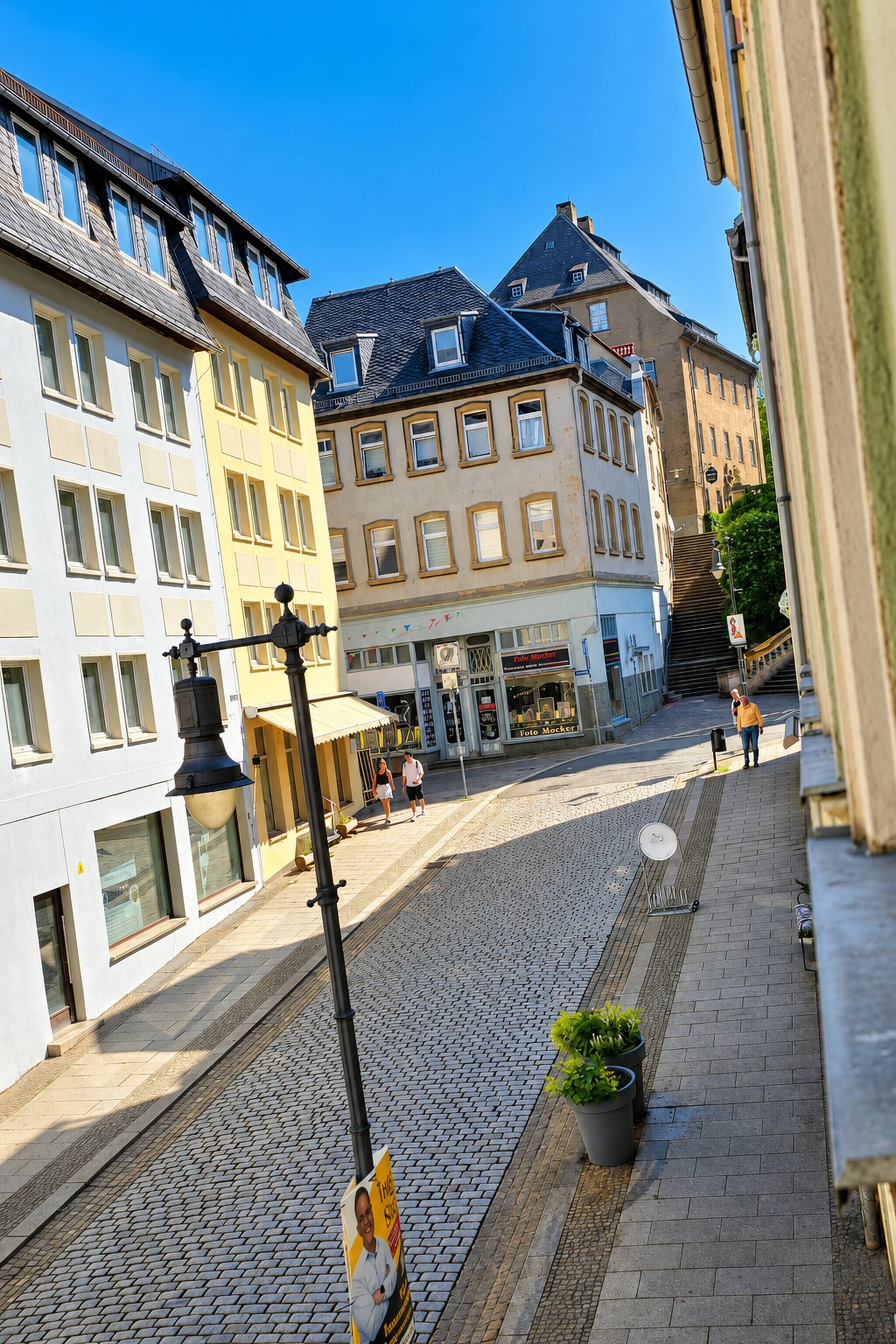 A cobblestone street with buildings on either side, a street lamp, and a sign for a photography studio.