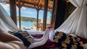 Una cama con vista a una piscina y zona de estar exterior, techo de madera y almohada roja con la etiqueta 'Variation 1'.