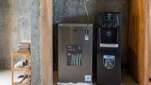 Un refrigerador GEA y un dispensador de agua en una habitación con pared de concreto y paneles de madera.