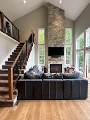 Ein geräumiges Wohnzimmer mit einer großen Eckcouch, einem Kamin, einem Flachbildfernseher und einer Treppe mit Holzgeländern.