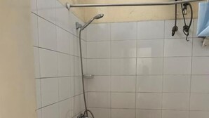 Pieni, laatoitettu kylpyhuone, jossa on wc, suihku ja pyyheteline.
