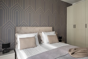 Un dormitorio con cama, dos mesitas de noche, un armario y papel tapiz estampado.