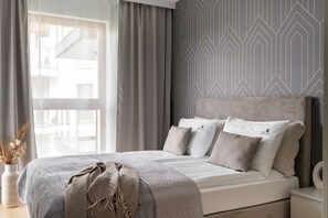 A bedroom with a bed, pillows, a bedside table, and a wall with geometric patterns. - Porto Mare Seaside with Parking and Gym (Gdańsk)