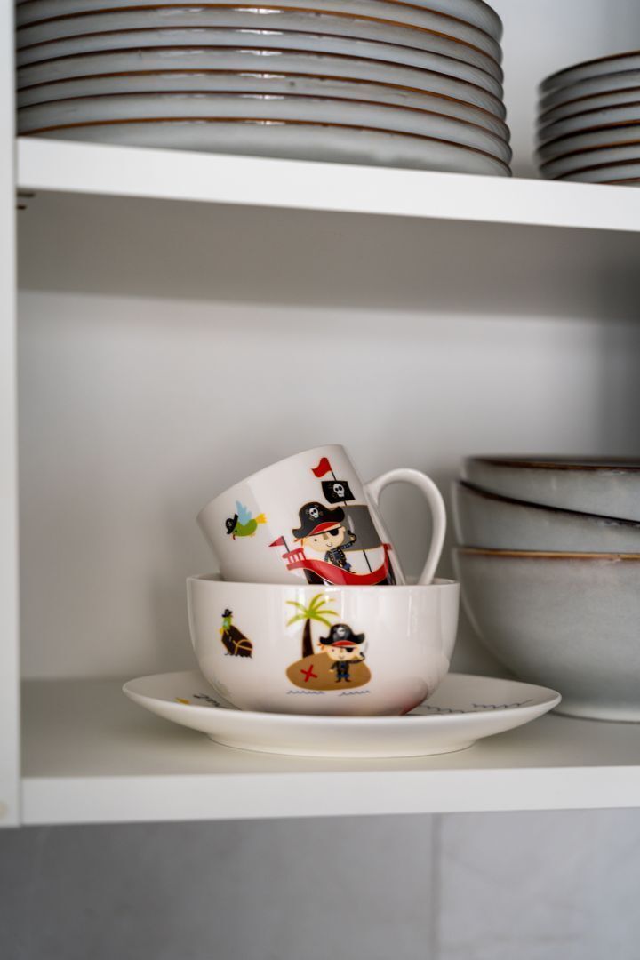 A stack of white ceramic plates and a mug with a pirate-themed design on a shelf.