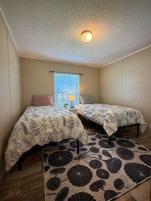 Un dormitorio con dos camas, una ventana con persianas, una lámpara de techo y una alfombra estampada.