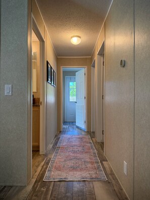 Un pasillo con alfombra estampada, suelo de madera y una puerta que da a una habitación con ventana.