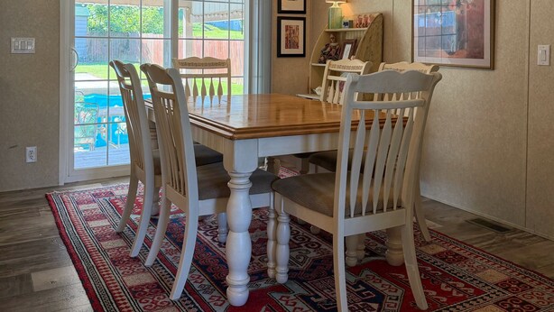 Un comedor con una mesa y sillas de madera, un tapete estampado y vistas a un espacio exterior a través de un ventanal.