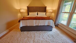 Quarto com cama grande, duas luminárias de cabeceira, janela com cortinas e vista para o verde lá fora.