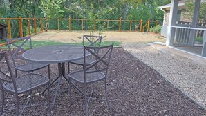 Uma área de pátio com mesa e cadeiras de metal, cercada por um portão de madeira e árvores.