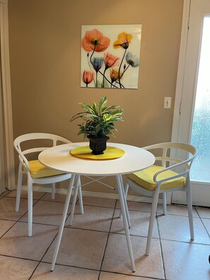 A dining area with a round table, two chairs, a potted plant, and a painting on the wall. - Pedal Inn 9-Economy Unit in a Convenient Location (Bentonville)