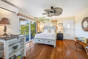 A bedroom with a bed, a desk, a chair, a ceiling fan, and a door. - Marjorie Kauai Inn (Lawai)