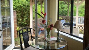 A room with a glass table, a chair, a vase with flowers, and a lamp. - Marjorie Kauai Inn (Lawai)