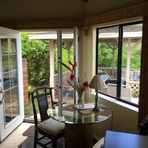 A room with a glass table, a chair, a vase with flowers, and a lamp. - Marjorie Kauai Inn (Lawai)