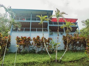 A two-story building with a blue exterior and a red roof, surrounded by lush greenery.