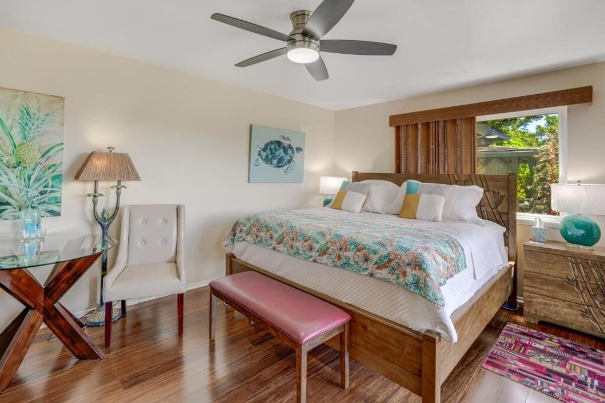A bedroom with a bed, a desk, a chair, a bench, a ceiling fan, and a window with a view.