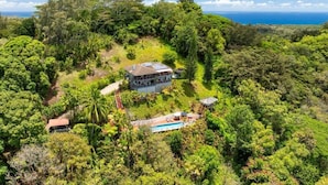 A house surrounded by dense tropical vegetation, with a clear view of the ocean in the background. - Marjorie Kauai Inn (Lawai)