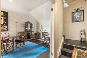 A room with a high ceiling, a staircase, a mirror, wicker furniture, and a fire extinguisher. - GuestReady - Charming Fulham Retreat with Balcony (London)