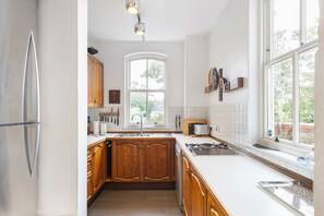 A kitchen with wooden cabinets, a stainless steel refrigerator, a window, and a tiled backsplash. - GuestReady - Charming Fulham Retreat with Balcony (London)