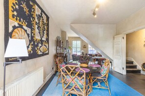 A dining area with a round table, wicker chairs, and a blue carpet. - GuestReady - Charming Fulham Retreat with Balcony (London)