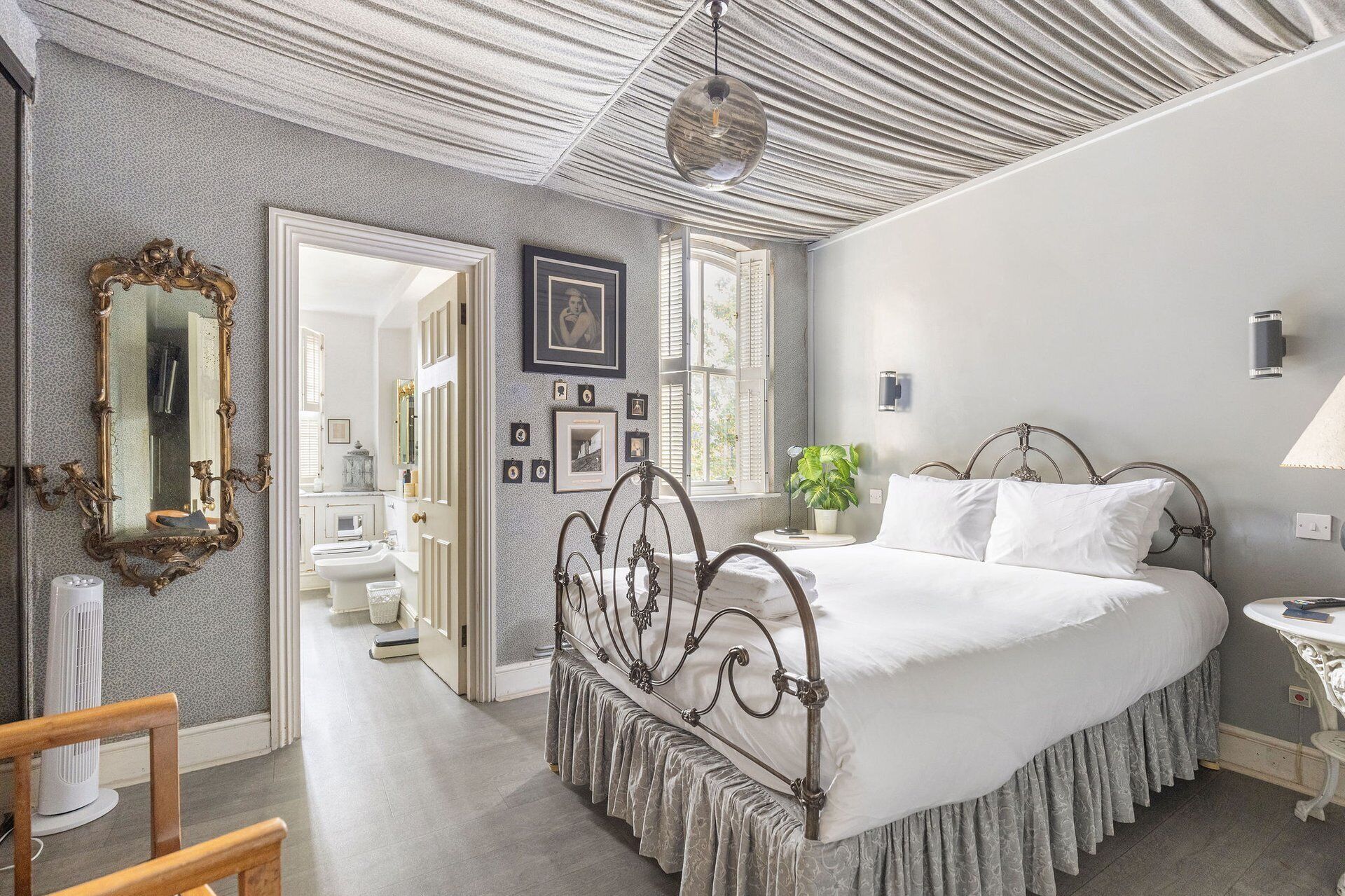 A bedroom with a bed, a mirror, a potted plant, and a wall-mounted lamp.