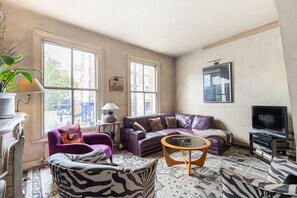 A living room with a leather sofa, armchairs, a coffee table, and a television. - GuestReady - Charming Fulham Retreat with Balcony (London)