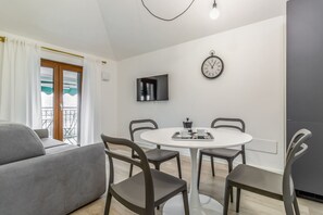 A modern living room with a sofa, a dining table with chairs, a flat-screen TV, and a wall clock. - Sporting by Wonderful Italy (Sirmione)