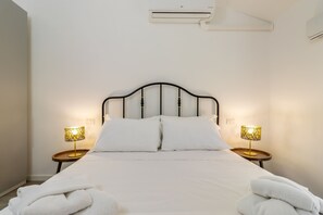 A neatly made bed with white linens, two bedside lamps with patterned shades, and a wall-mounted air conditioner. - Sporting by Wonderful Italy (Sirmione)