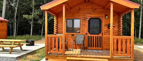 A wooden cabin with a porch, a picnic table, and a chair.