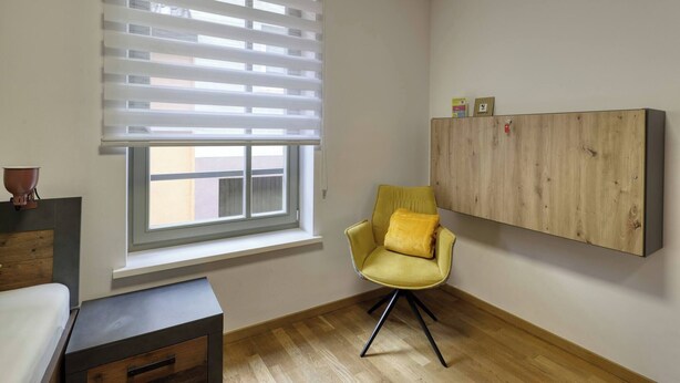 A room with a window, a yellow chair, a wooden cabinet, and a small table. - Holiday Home - Cityhouse WG9 - 6 Guests - 3BR (Marktheidenfeld)