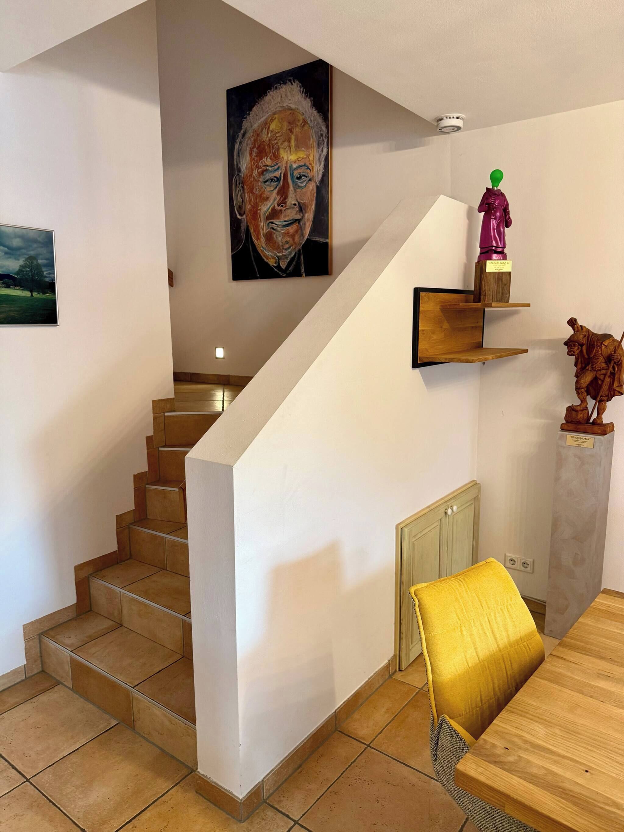 A staircase with a wooden finish, a painting on the wall, and a statue on the landing.