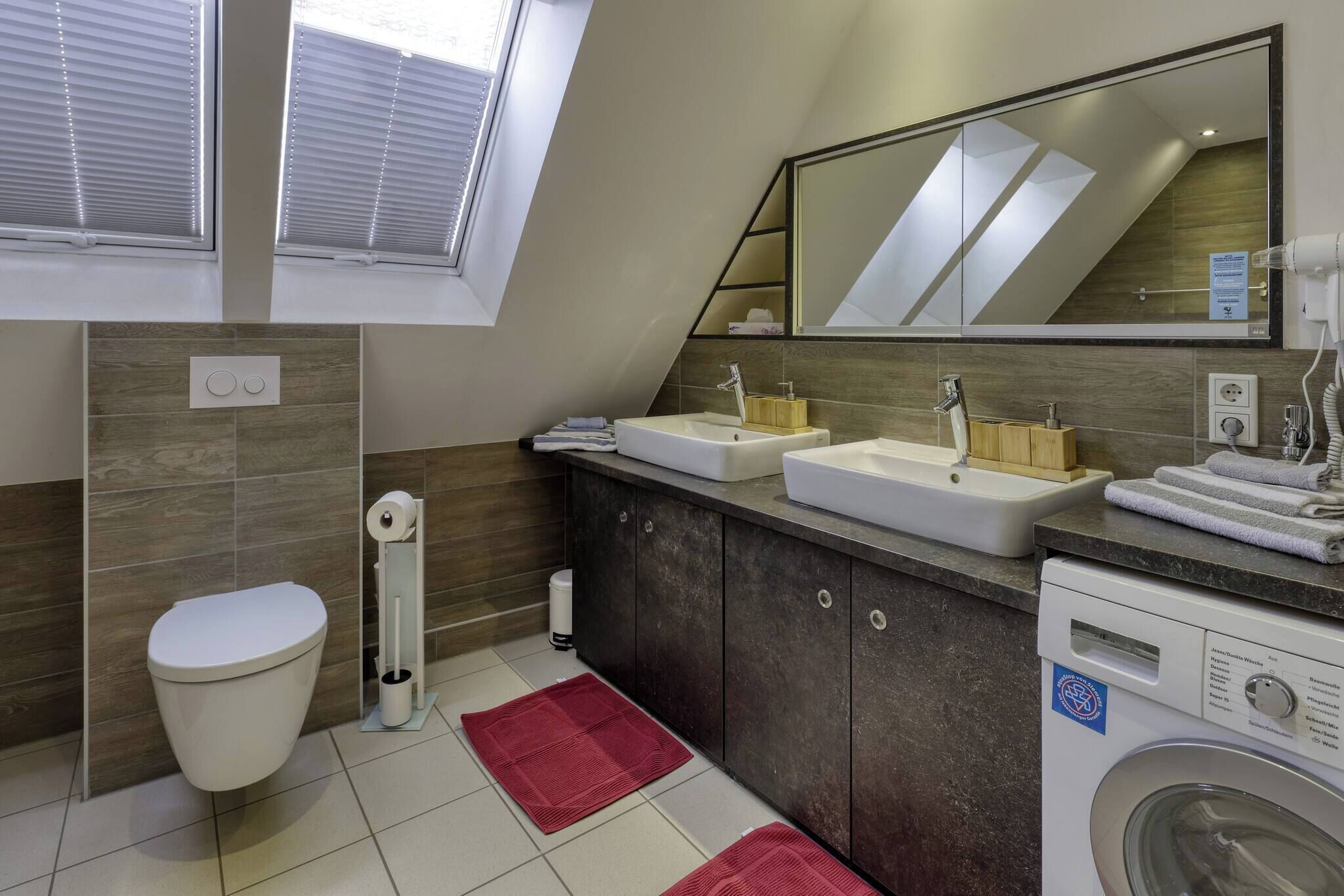 A modern bathroom with a toilet, sink, mirror, and washing machine.