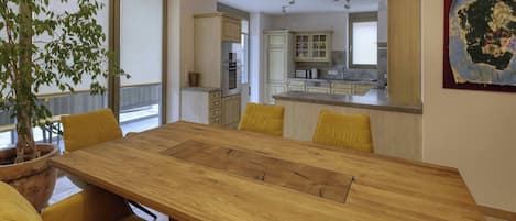 Une cuisine moderne avec des meubles blancs, un îlot central et un coin repas comprenant une table en bois et des chaises jaunes.