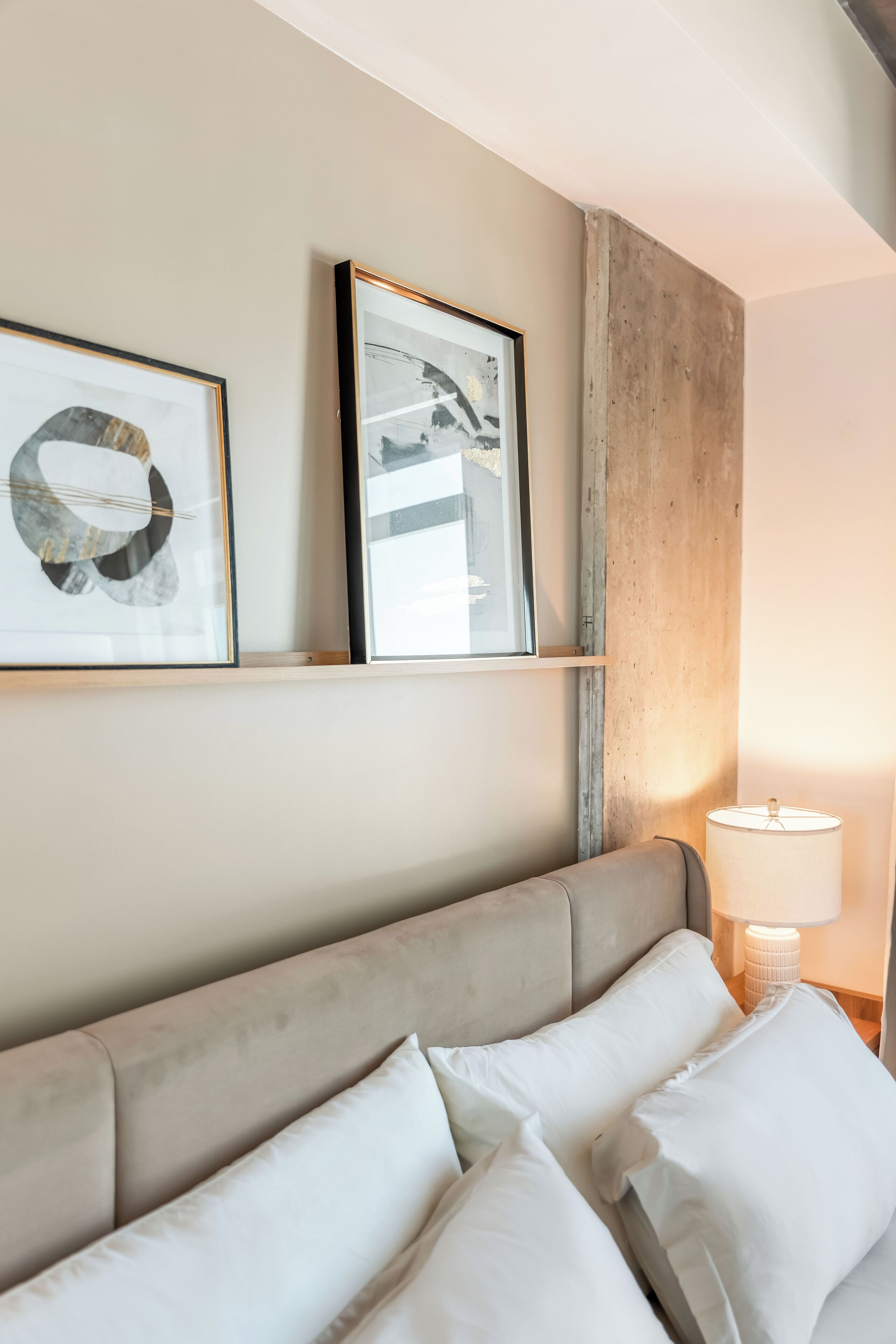Quarto de hotel com cama, mesa de cabeceira com abajur e duas obras de arte emolduradas na parede.