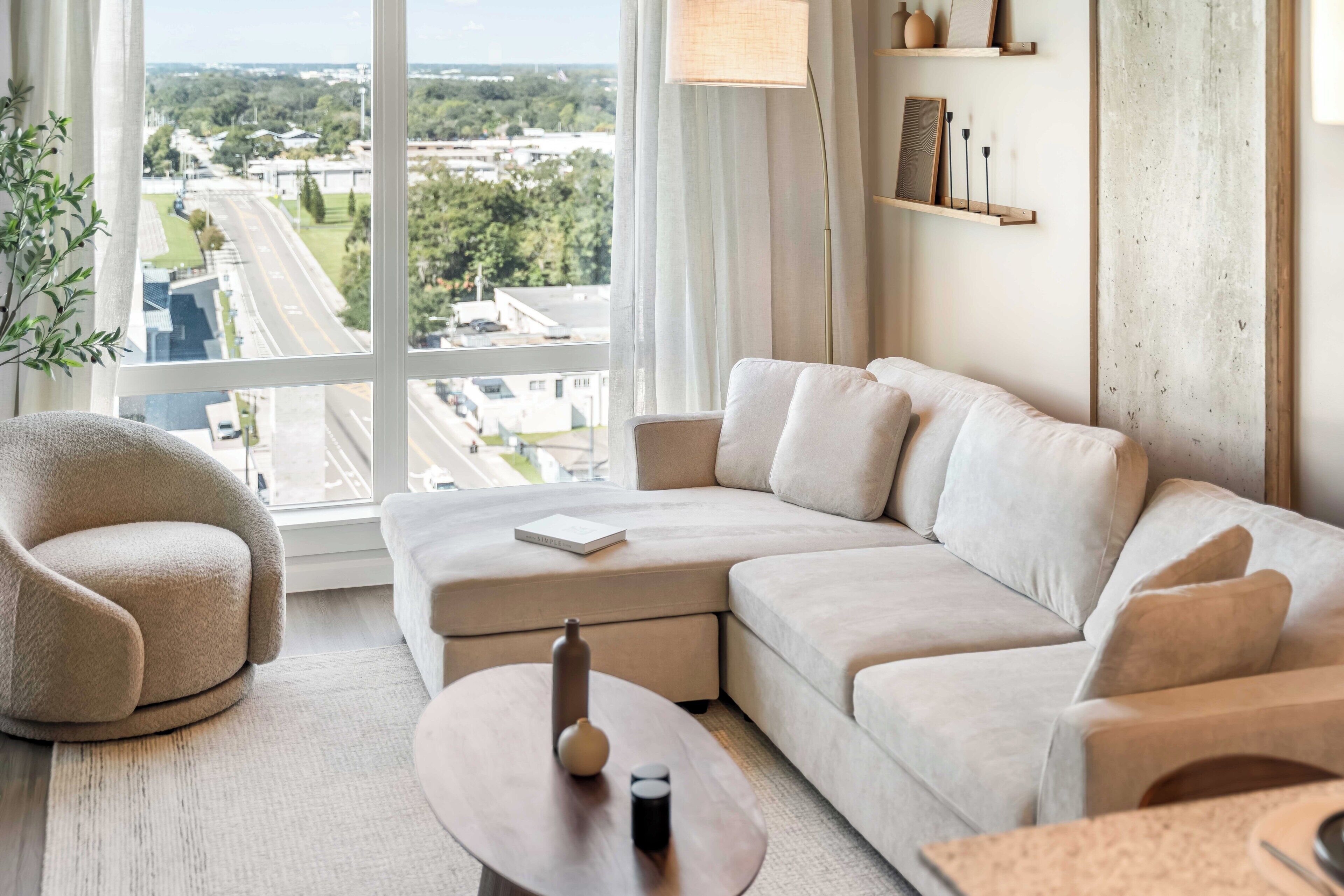 Una sala de estar moderna con un sofá modular, una mesa de centro redonda y vistas a un paisaje urbano a través de grandes ventanales.