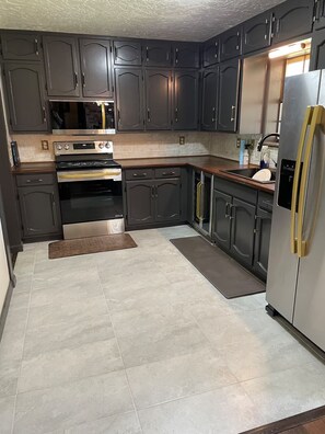 A kitchen with dark cabinets, stainless steel appliances, and a tiled floor. - Luxury & Group Focused  for families or friends. 4 bedrooms 3 full baths. (Attalla)