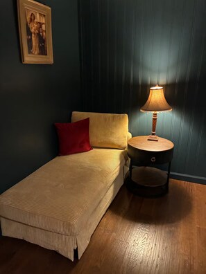 Ein Einzelbett mit einem roten Kopfkissen, ein kleiner Nachttisch mit Lampe und ein gerahmtes Bild an der Wand.