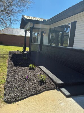A residential building with a covered porch, a brick foundation, and a landscaped garden area. - Luxury & Group Focused  for families or friends. 4 bedrooms 3 full baths. (Attalla)