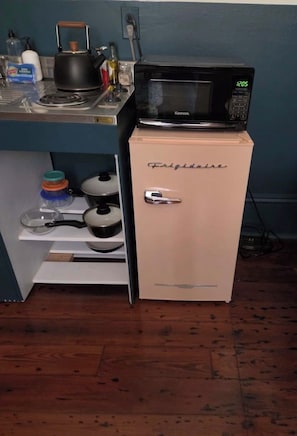 Eine kompakte Küche mit einer Mikrowelle auf dem Kühlschrank, einem Wasserkocher und verschiedenen Küchenutensilien auf der Arbeitsplatte.