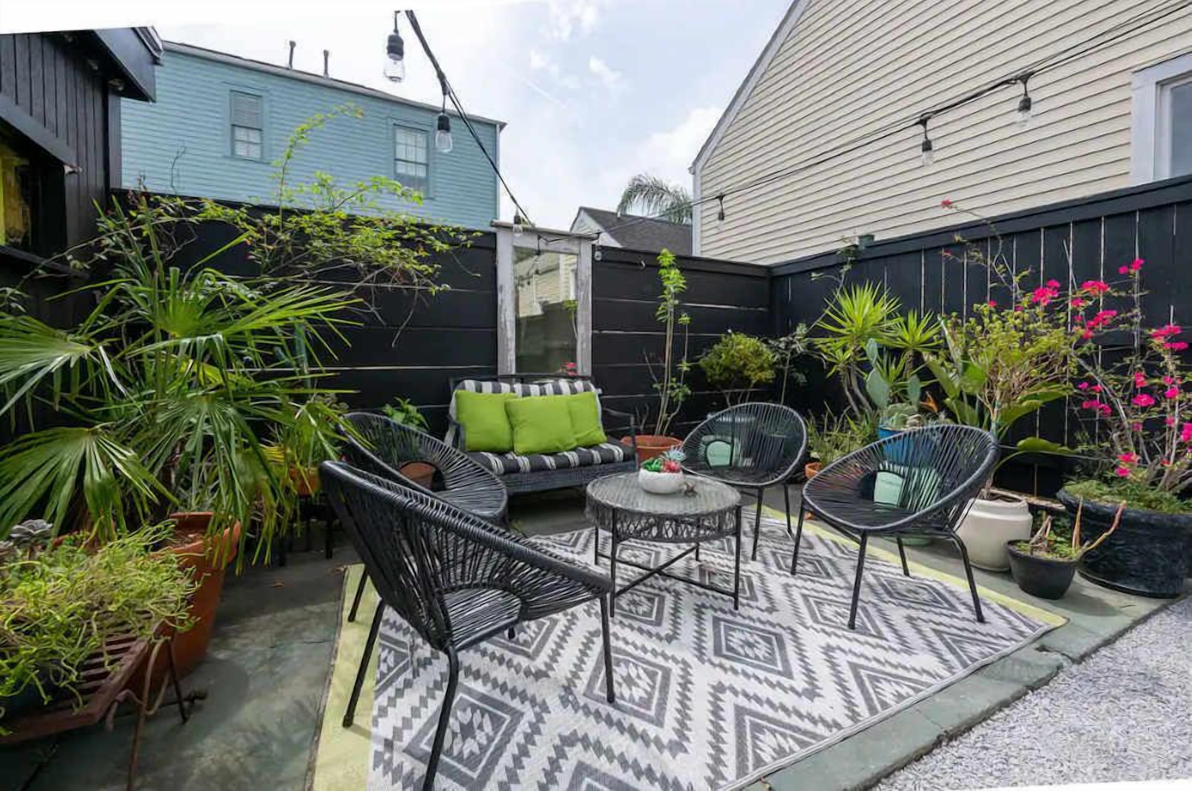 A patio area with outdoor furniture, including a sofa and chairs, surrounded by potted plants and a patterned rug.