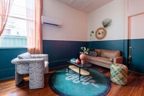 Une pièce comprenant un canapé, un fauteuil à motifs, une petite table avec un vase, un tapis rond et un climatiseur fixé au mur.