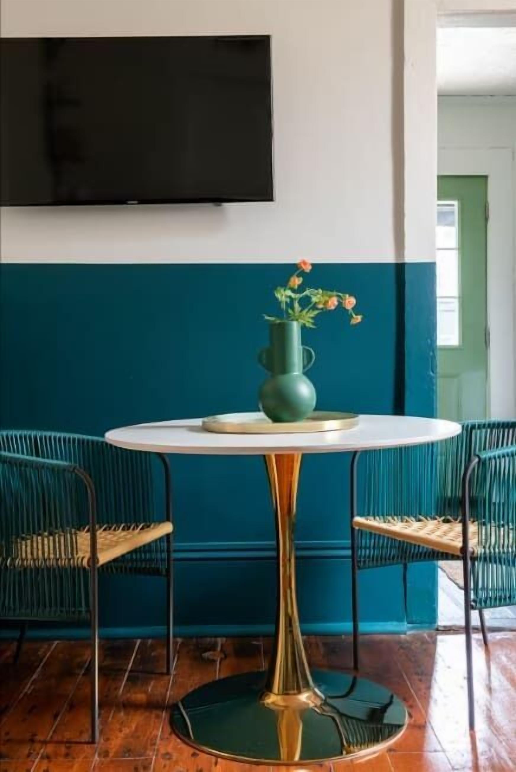 Una mesa redonda con un jarrón verde y flores, rodeada por cuatro sillas verdes.