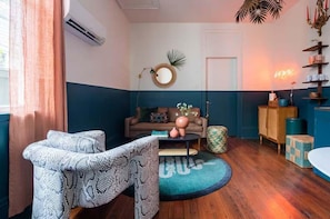 Une pièce comprenant un canapé, un fauteuil à motifs, une table basse ronde et un panneau lumineux néon.