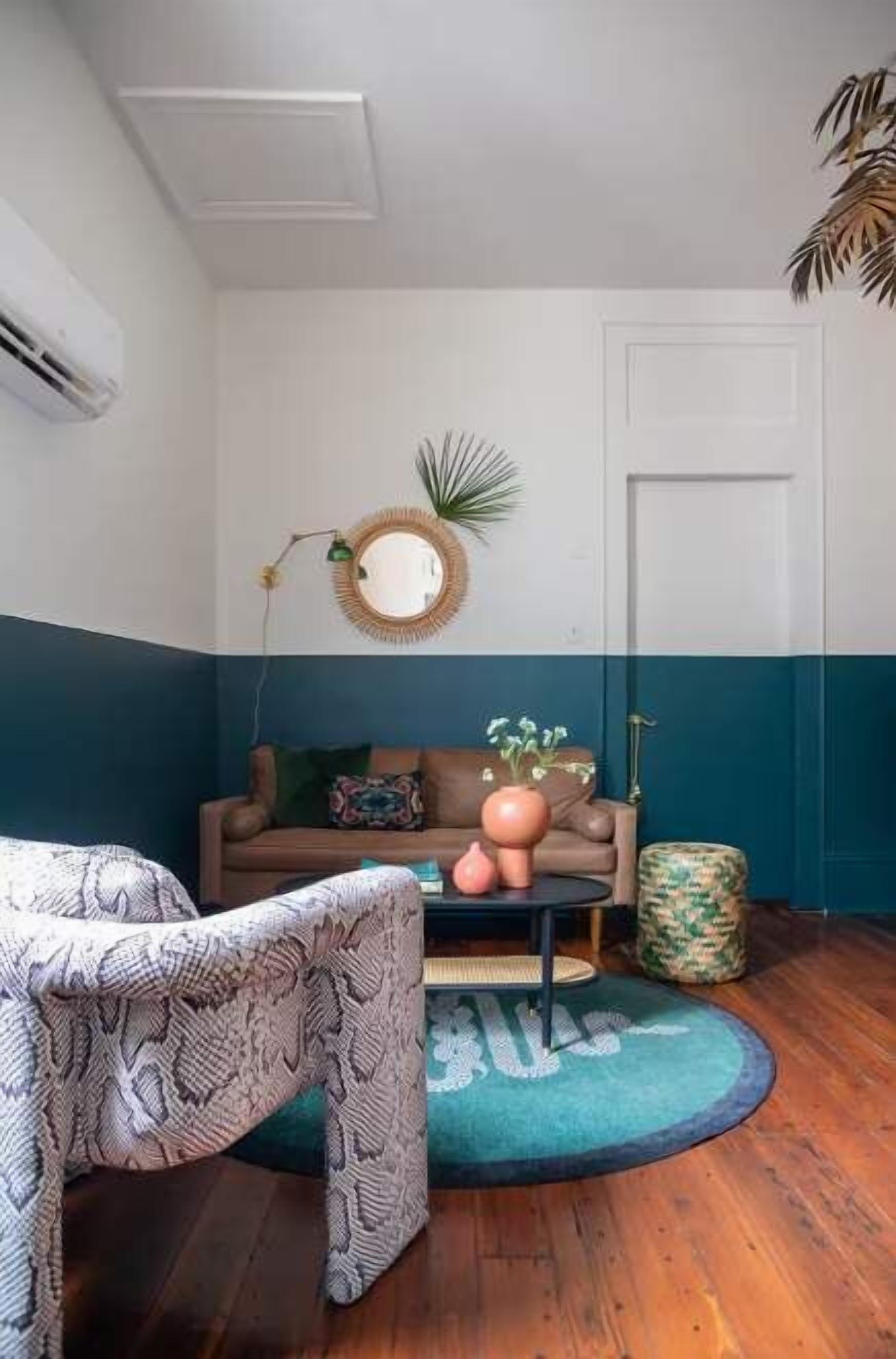 A room with a patterned chair, a sofa with cushions, a round mirror, and a door.